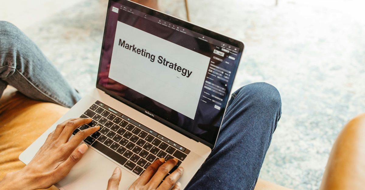 Laptopt auf den Beinen einer Person. Auf dem Screen steht gross "Marketing Strategie" geschrieben.